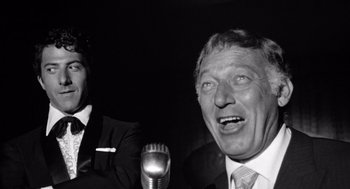 Movie still from “Lenny” (1974), directed by Bob Fosse – A man in a suit and a tie is talking into a microphone; Close Up shot, Low angle