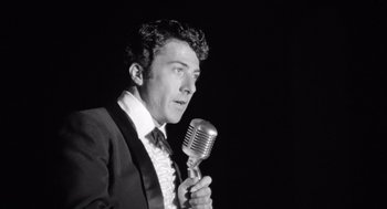 Movie still from “Lenny” (1974), directed by Bob Fosse – A black and white photo of a man holding a microphone; Close Up shot, Low angle