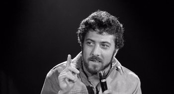 Movie still from “Lenny” (1974), directed by Bob Fosse – Black and white photograph of a man holding a microphone and gesturing; Close Up shot, Low angle