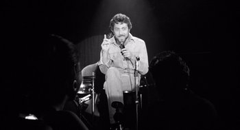 Movie still from “Lenny” (1974), directed by Bob Fosse – A black and white photo of a man holding a microphone; Medium shot, Low angle