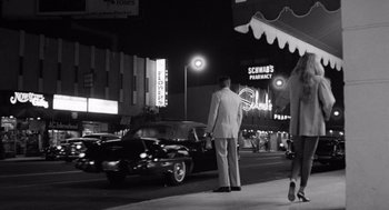 Movie still from “Lenny” (1974), directed by Bob Fosse – A black and white photo of a man standing on the side of the street; Wide shot, Low angle