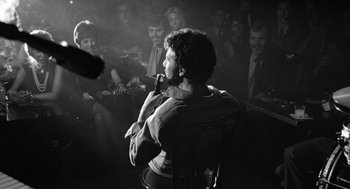 Movie still from “Lenny” (1974), directed by Bob Fosse – A group of people sitting in a dark room; Medium shot, Over the shoulder angle