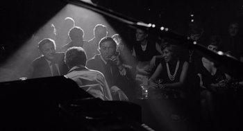 Movie still from “Lenny” (1974), directed by Bob Fosse – A group of people sitting in a dark room next to each other; Medium shot, High angle
