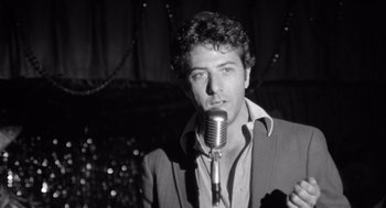 Movie still from “Lenny” (1974), directed by Bob Fosse – A black and white photo of a man singing into a microphone; Close Up shot, Over the shoulder angle