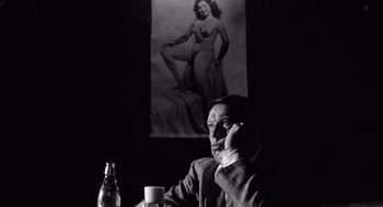 Movie still from “Lenny” (1974), directed by Bob Fosse – A man sitting at a table with a beer in front of him; Medium shot, Low angle