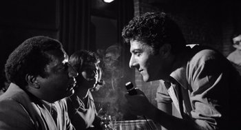 Movie still from “Lenny” (1974), directed by Bob Fosse – A man smoking a cigarette while talking to two other men; Medium shot, Low angle