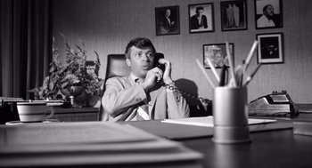 Movie still from “Lenny” (1974), directed by Bob Fosse – A man sitting at a desk talking on a phone; Medium shot, High angle