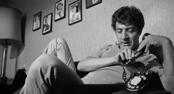 Movie still from “Lenny” (1974), directed by Bob Fosse – A man sitting on a couch talking on a phone; Close Up shot, Low angle