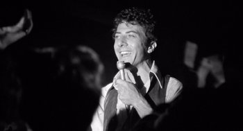 Movie still from “Lenny” (1974), directed by Bob Fosse – A black and white photo of a man holding a microphone; Close Up shot, Low angle