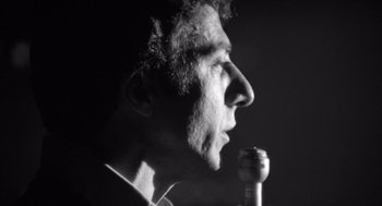Movie still from “Lenny” (1974), directed by Bob Fosse – A black and white photo of a man speaking into a microphone; Close Up shot, Low angle