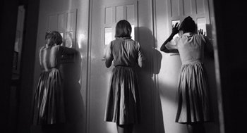 Movie still from “Lenny” (1974), directed by Bob Fosse – A woman standing in front of a door and looking in a mirror; Medium shot, Low angle
