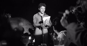 Movie still from “Lenny” (1974), directed by Bob Fosse – A man standing in front of a microphone and holding papers; Medium shot, Low angle