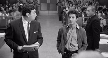 Movie still from “Lenny” (1974), directed by Bob Fosse – Two men in suits stand in front of an audience; Medium shot, Over the shoulder angle
