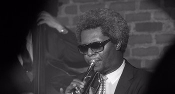 Movie still from “Lenny” (1974), directed by Bob Fosse – A black and white photo of a man playing the trumpet; Close Up shot, Low angle