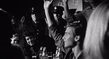 Movie still from “Lenny” (1974), directed by Bob Fosse – A black and white photo of a group of people sitting at a table; Medium shot, Over the shoulder angle