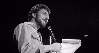 Movie still from “Lenny” (1974), directed by Bob Fosse – A man is speaking at a podium while holding a microphone; Close Up shot, Low angle