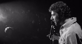 Movie still from “Lenny” (1974), directed by Bob Fosse – A black and white photo of a man speaking into a microphone in front of a group of people; Close Up shot, Low angle