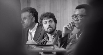 Movie still from “Lenny” (1974), directed by Bob Fosse – A black - and - white photo of three men sitting at a table; Medium shot, Low angle