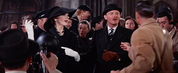 Movie still from “Les Girls” (1957), directed by George Cukor – A group of people in suits and hats singing together; Medium shot, Over the shoulder angle