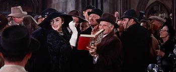 Movie still from “Les Girls” (1957), directed by George Cukor – A group of people wearing hats and holding a book; Medium shot, Low angle