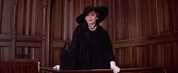 Movie still from “Les Girls” (1957), directed by George Cukor – A woman wearing a black hat and a black coat; Medium shot, Low angle