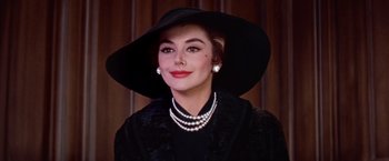 Movie still from “Les Girls” (1957), directed by George Cukor – A woman wearing a black hat and a black coat; Close Up shot, Low angle