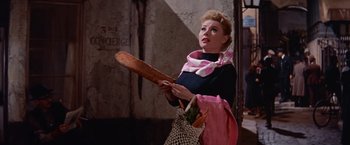Movie still from “Les Girls” (1957), directed by George Cukor – A woman holding a wooden spoon and a bag of food; Medium shot, Low angle