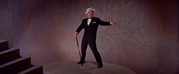 Movie still from “Les Girls” (1957), directed by George Cukor – A man in a suit and hat holding a cane; Medium shot, Low angle