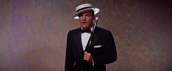 Movie still from “Les Girls” (1957), directed by George Cukor – A man in a suit and hat holding a baseball bat; Medium shot, Low angle