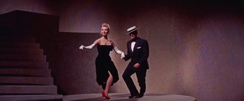 Movie still from “Les Girls” (1957), directed by George Cukor – A man and a woman in a black dress and white gloves; Wide shot, Low angle