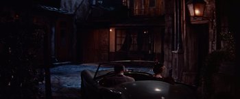 Movie still from “Les Girls” (1957), directed by George Cukor – A man and a woman sitting in the back of a car; Wide shot, High angle