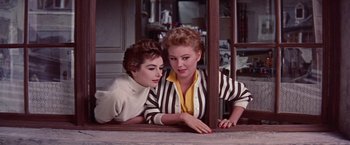 Movie still from “Les Girls” (1957), directed by George Cukor – Two women leaning on a table in a room; Medium shot, Low angle