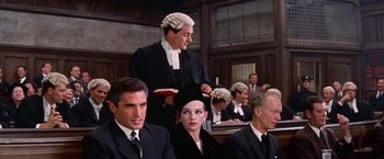 Movie still from “Les Girls” (1957), directed by George Cukor – A man in a courtroom with a woman in a wig; Medium shot, High angle