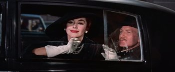 Movie still from “Les Girls” (1957), directed by George Cukor – An older woman waves from a car while a younger man looks on; Close Up shot, Low angle