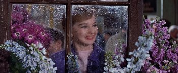 Movie still from “Les Girls” (1957), directed by George Cukor – A woman looking out of a window at a crowd of onlookers; Close Up shot, Over the shoulder angle