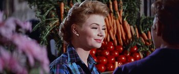 Movie still from “Les Girls” (1957), directed by George Cukor – A woman in plaid shirt standing in front of a bunch of vegetables; Close Up shot, Over the shoulder angle
