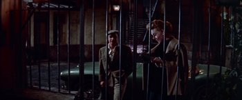 Movie still from “Les Girls” (1957), directed by George Cukor – A man and a woman standing next to each other in front of a green car; Medium shot, High angle