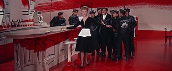 Movie still from “Les Girls” (1957), directed by George Cukor – A group of men and women in uniform and a woman in a black dress; Medium shot, Low angle