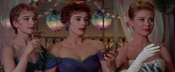 Movie still from “Les Girls” (1957), directed by George Cukor – A woman in a purple and green dress holding a glass of wine; Close Up shot, Over the shoulder angle