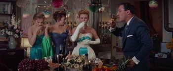 Movie still from “Les Girls” (1957), directed by George Cukor – A group of people standing around a table with food; Medium shot, Low angle