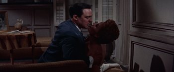 Movie still from “Les Girls” (1957), directed by George Cukor – A man and a woman kissing on a couch in front of a window; Medium shot, Low angle