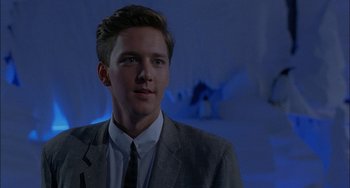 Movie still from “Less Than Zero” (1987), directed by Marek Kanievska – A man in a suit and tie in front of a blue background; Close Up shot, Low angle