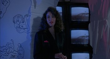 Movie still from “Less Than Zero” (1987), directed by Marek Kanievska – A woman in a black jacket standing in front of a window; Medium shot, Low angle