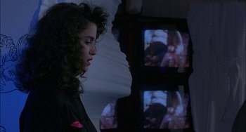 Movie still from “Less Than Zero” (1987), directed by Marek Kanievska – A woman standing in front of a television screen; Close Up shot, Over the shoulder angle