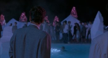 Movie still from “Less Than Zero” (1987), directed by Marek Kanievska – A crowd of people standing around a pool at night; Wide shot, Over the shoulder angle