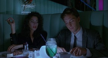 Movie still from “Less Than Zero” (1987), directed by Marek Kanievska – A man and a woman sitting at a table in front of a drink; Medium shot, High angle