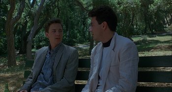 Movie still from “Less Than Zero” (1987), directed by Marek Kanievska – Two young men sitting on a park bench talking to each other; Medium shot, Over the shoulder angle