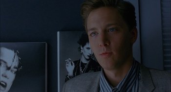 Movie still from “Less Than Zero” (1987), directed by Marek Kanievska – A man in a suit and tie in front of a picture of a woman smoking a cigarette; Close Up shot, Over the shoulder angle