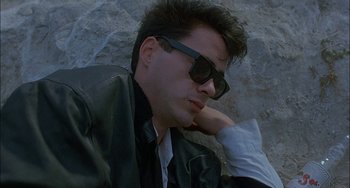 Movie still from “Less Than Zero” (1987), directed by Marek Kanievska – A man wearing sunglasses and a leather jacket leaning against a rock; Close Up shot, Low angle