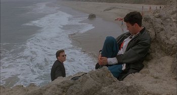Movie still from “Less Than Zero” (1987), directed by Marek Kanievska – Two men sitting on a rock near the ocean; Wide shot, Low angle